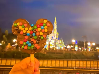 Mickey shaped cereal treat covered in chocolate and m&m candies with the Magic kingdom castle in the background at Disney World