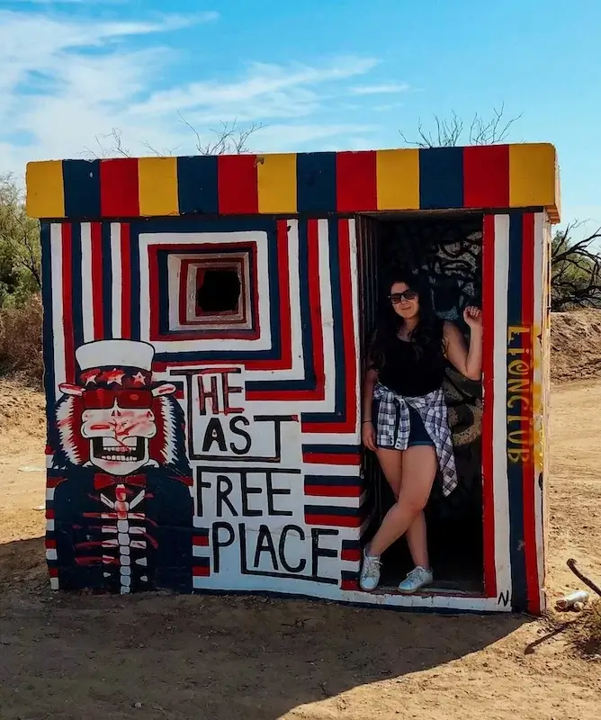 Elaina standing next to a painting that is located at the entrance of Slab city and claims it to be "the last free place"