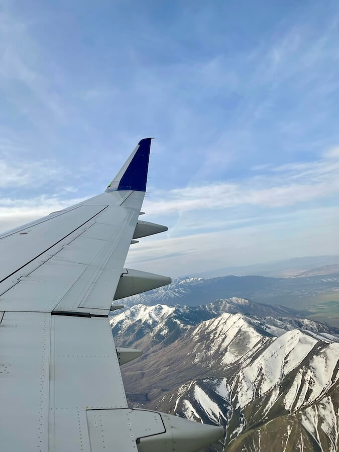 The view out of an airplane window of the plane wing and snowcapped mountains below