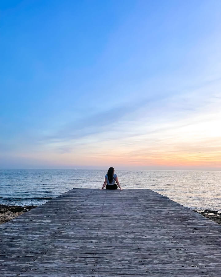 Elaina sitting on a dock with her back to the camera looking out over the ocean