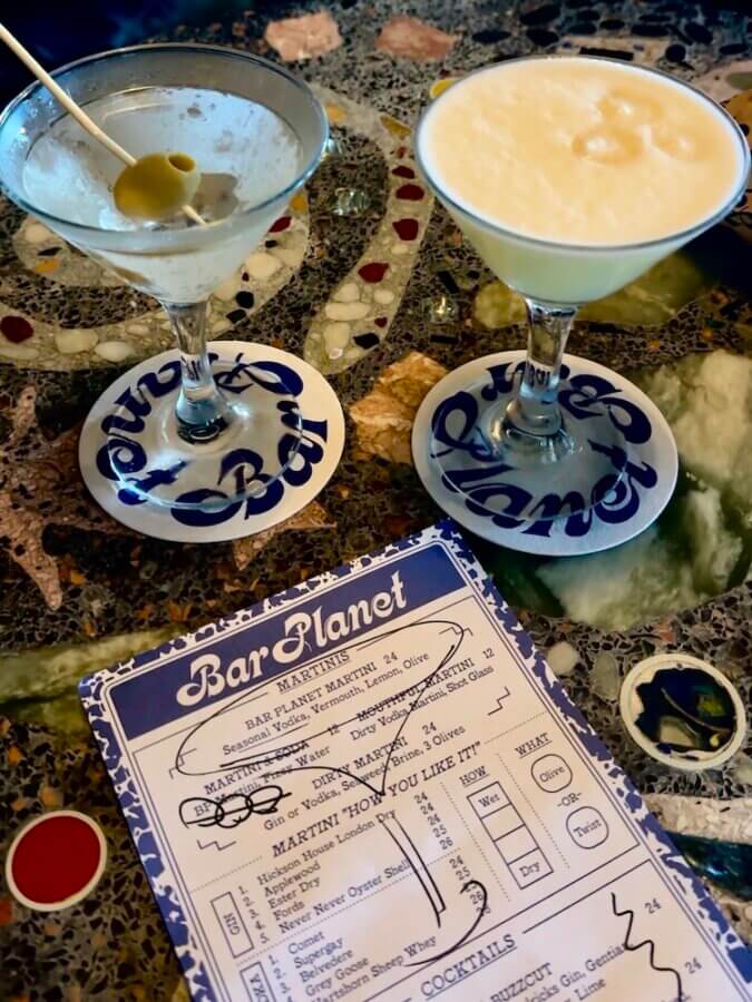 A regular martini, a breakfast martini, and a menu sitting on a colorful table at Bar Planet cocktail bar in Newtown, Sydney