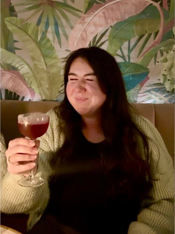 Elaina holding her drink in front of a pink and green wall at Maybe Sammy cocktail bar in Sydney