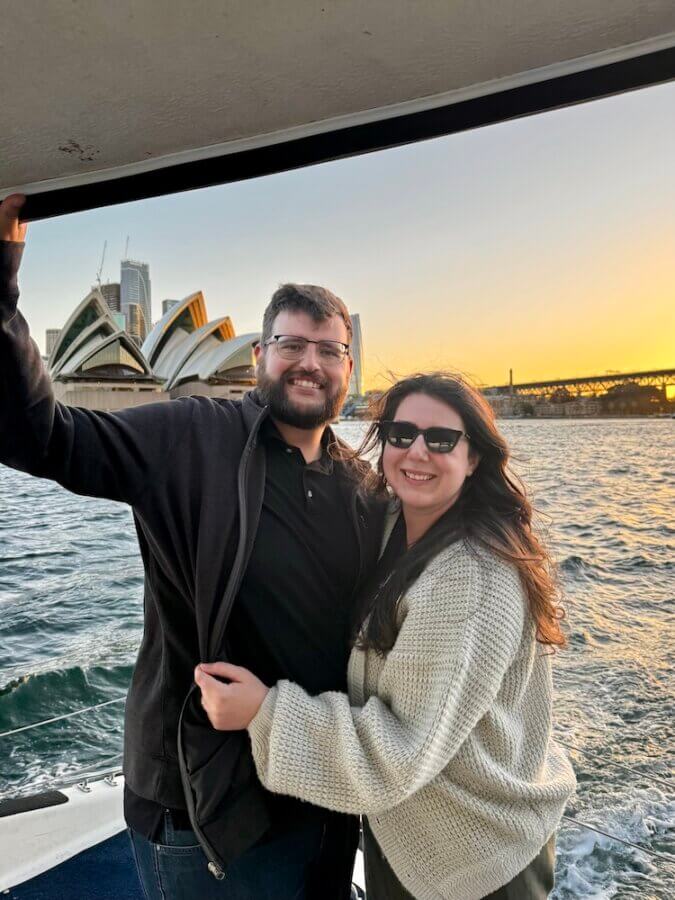 Elaina and Zac on a BYO Sydney Harbour cruise at sunset with the harbour bridge and Sydney Opera House in the background